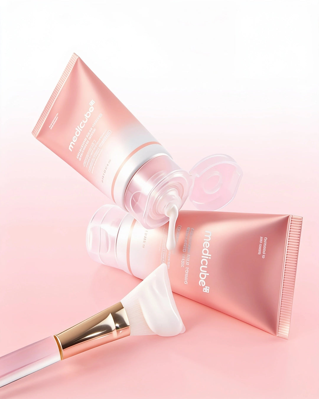 Three pink Medcube skincare tubes and a spatula brush arranged on a soft pink background, with one tube open and cream being dispensed.