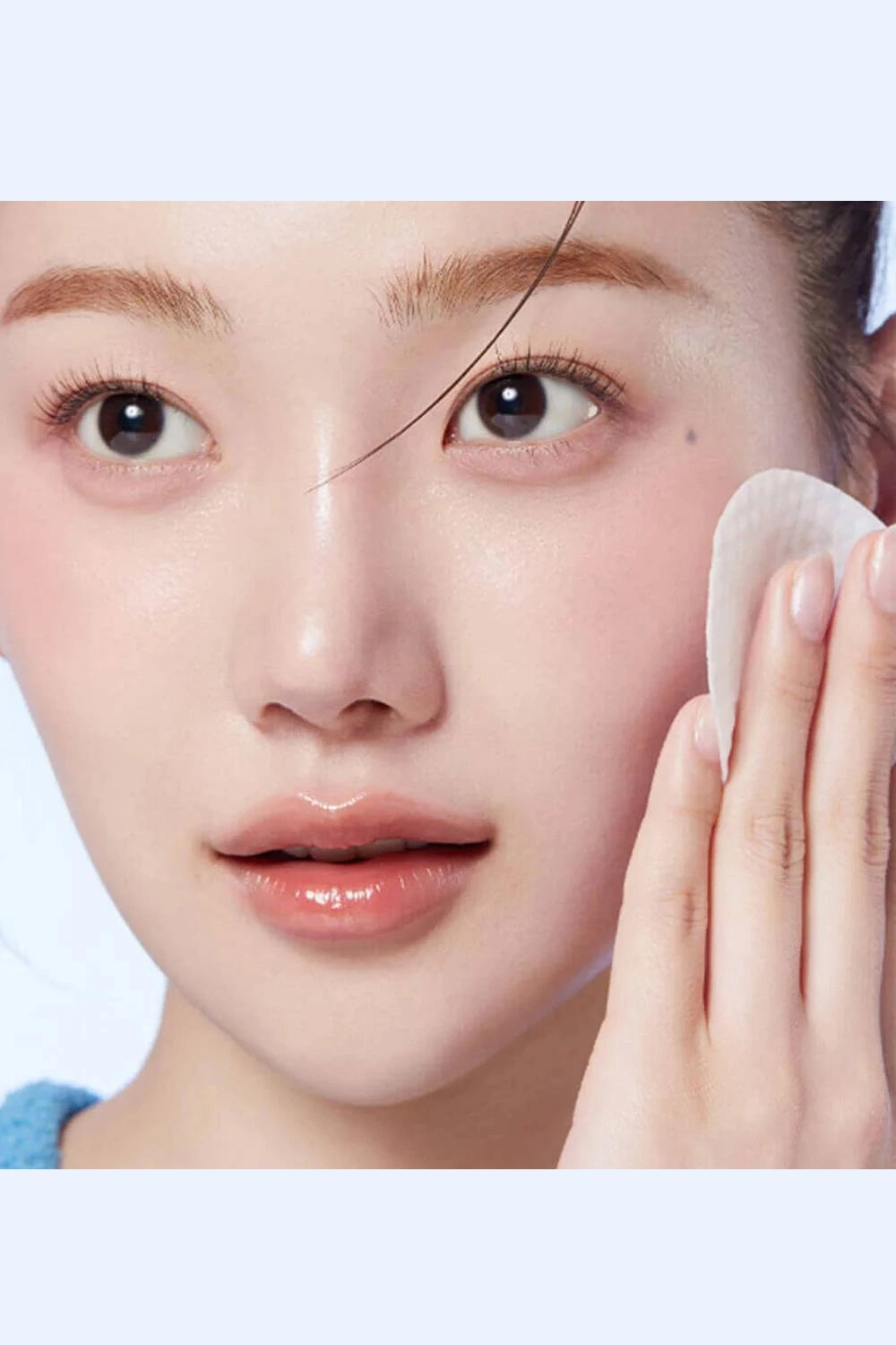 Close-up of a person using a cotton pad on their face with a plain background