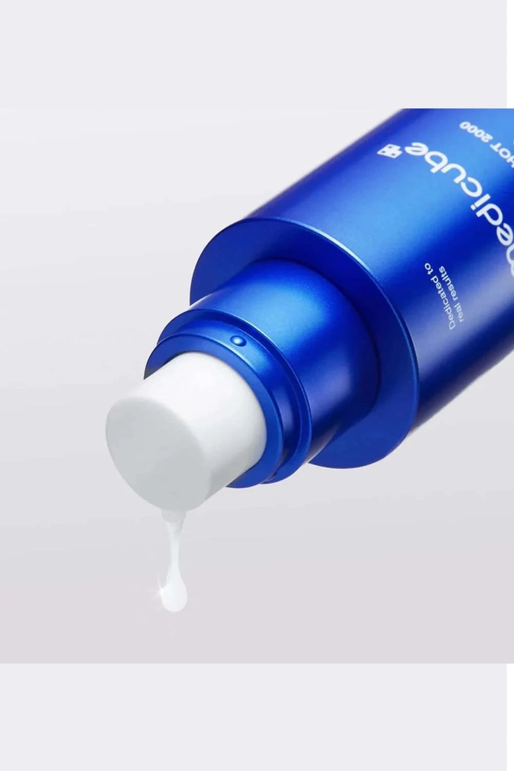 Blue skincare bottle with white cream being squeezed out on a light gray background