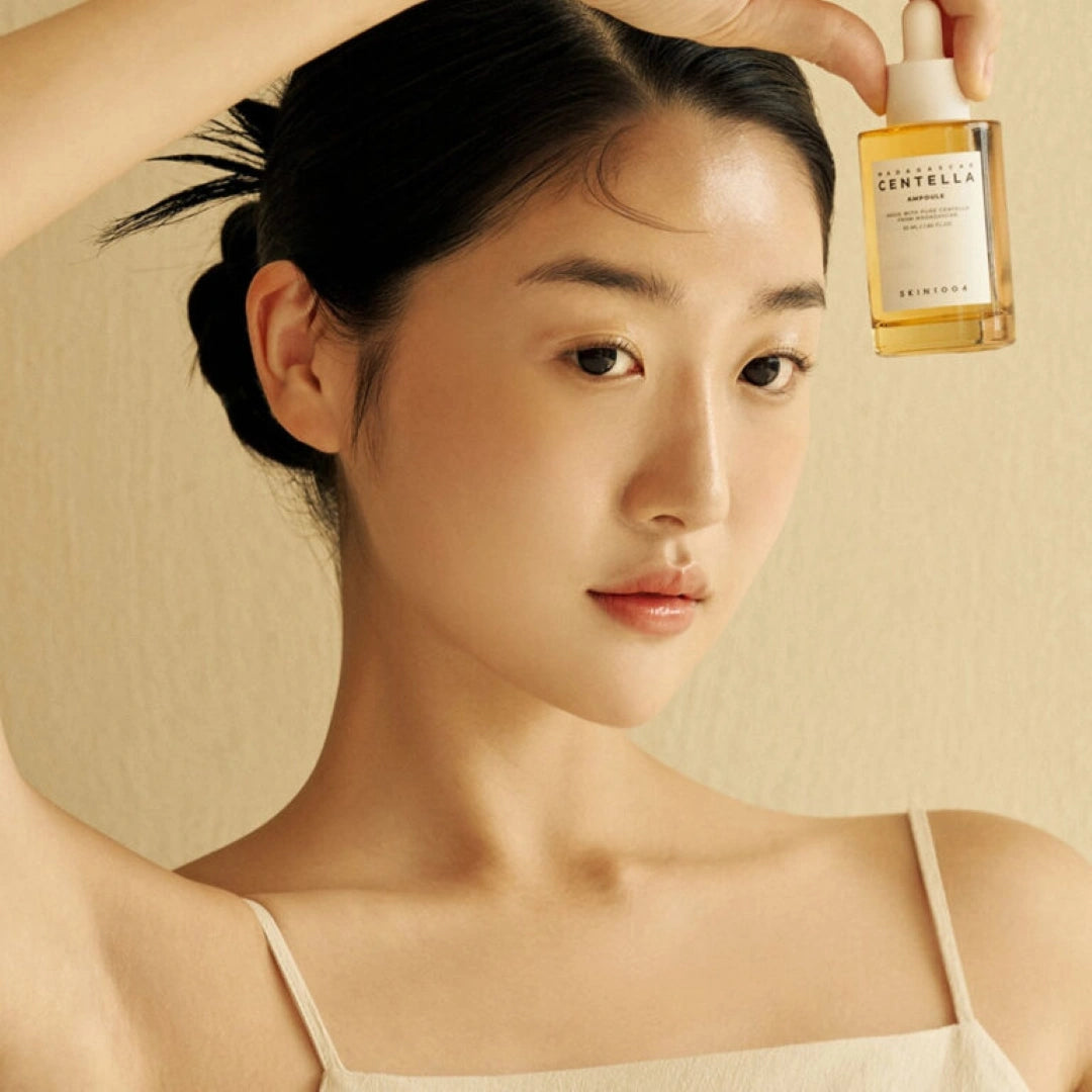 Woman holding a bottle of Centella Asiatica product against a beige background