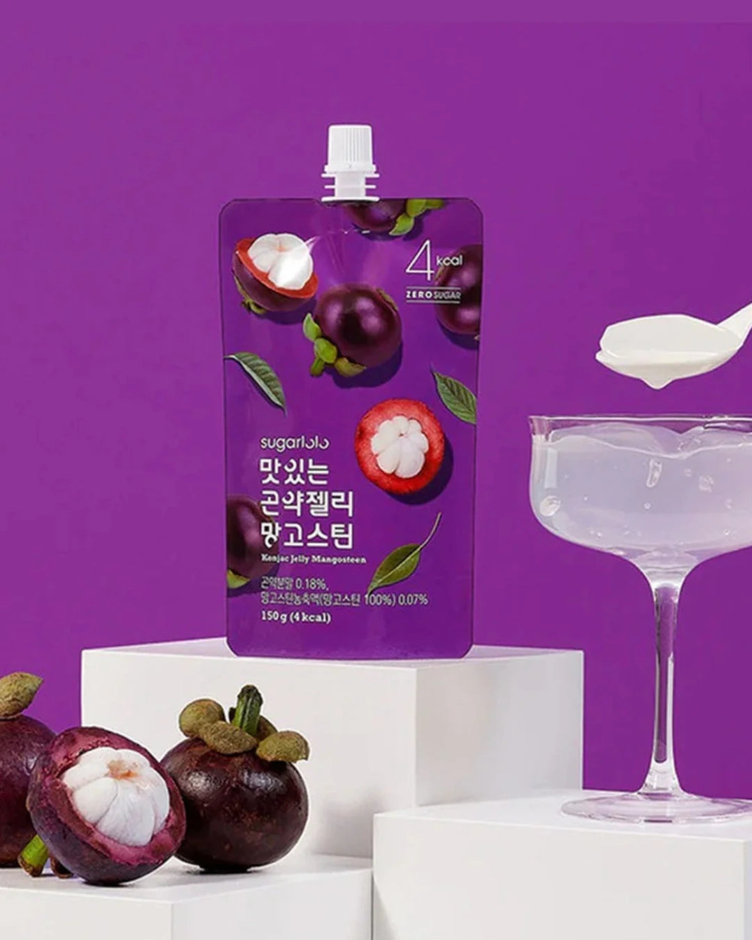 A purple stand-up pouch of sugartalk mangosteen-flavored sugar syrup stands on white display blocks, with real mangosteens and a glass coupe filled with clear syrup beside it against a solid purple background.