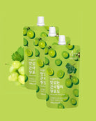 Three sugarlab grape juice pouches arranged in a fan shape on a light green background, with a bunch of green grapes on the left side. The pouches are light green with a pattern of green grapes and white caps.