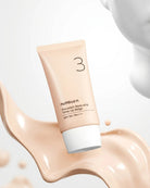 A squeeze tube of numbuz-n Porcelain Base-skip Tone Up Beige SPF 50+ PA+++ cosmetic product floating over a glossy beige makeup smear, with a white abstract head shape in the background.