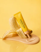 A yellow squeeze tube labeled BANANA PORN and 'KOREAN SKIN CARE' is styled with a peeled banana and a smear of beige cream on a yellow background.