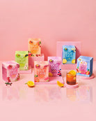 A collection of colorful 'our tea' tea boxes in various flavors, arranged on pink pedestals against a solid pink background, with a glass of iced tea and lemon slices in the foreground.