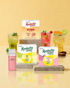 Teazen Kombucha beverage products displayed on a warm beige studio background, including boxed tea products, a small bottle, and three colorful drinks with fruit garnishes and ice.