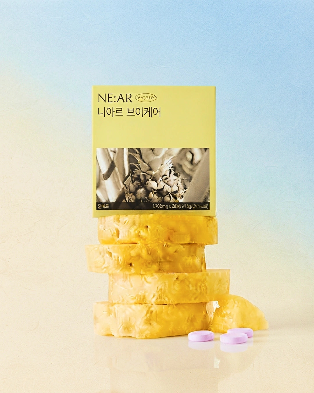 A stack of yellow-orange gummy candies with a pale yellow NE:AR brand card standing behind them, plus three small lavender round gummies in front, set against a soft blue-to-beige gradient background.