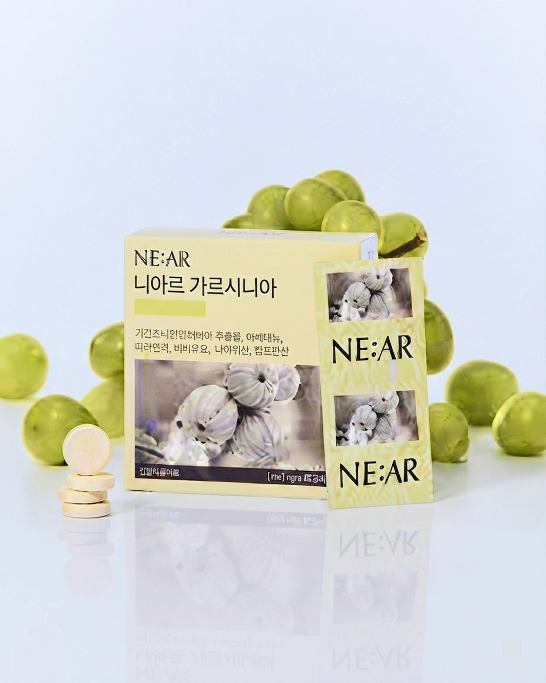NE:AR niacin supplement packaging with a pale yellow box and sachet, surrounded by green grapes and a few round beige tablets on a clean white reflective surface.