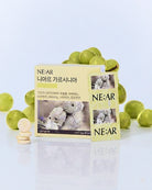 NE:AR niacin supplement packaging with a pale yellow box and sachet, surrounded by green grapes and a few round beige tablets on a clean white reflective surface.