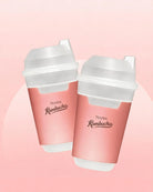Two pink reusable travel cups with white lids and spouts, printed with the text 'TEAZEN Kombucha', shown on a soft pink background.