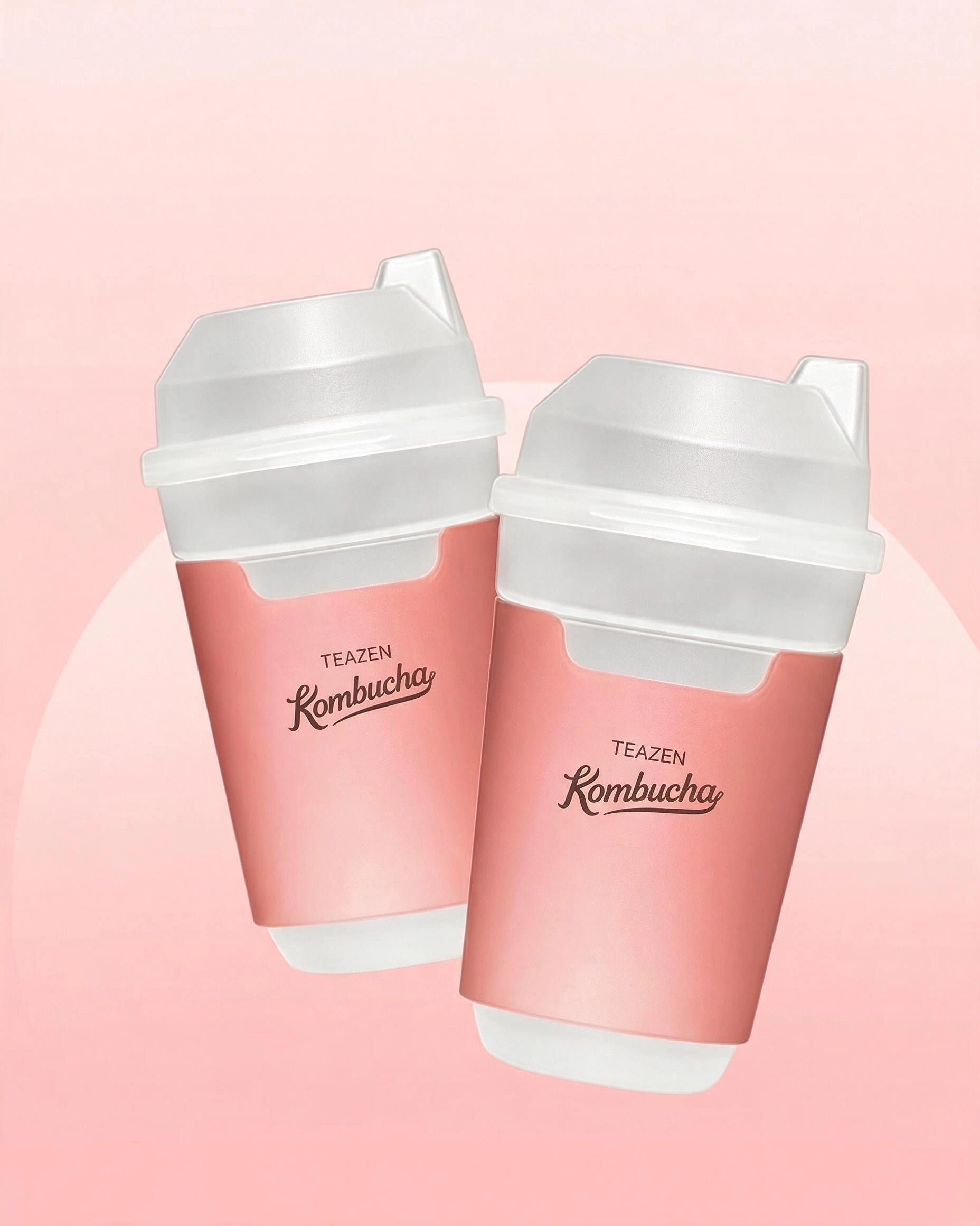 Two pink reusable travel cups with white lids and spouts, printed with the text 'TEAZEN Kombucha', shown on a soft pink background.