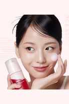Woman applying cream to her face with a skincare product in the foreground