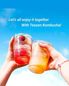 Two hands holding clear plastic cups filled with colorful tea-based drinks, one red and one orange, against a bright blue sky background. White text at the top reads, 'Let's all enjoy it together With Teazen Kombucha!'.
