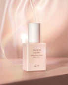 A square bottle of Kows Bloom Glow Essence Sun Cream SPF30 PA++++ with a white cap, set against a soft, warm pink and beige background with elegant light streaks.