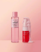 Two Medik8 skincare bottles on a soft pink studio background: a tall translucent pink bottle labeled 'Medik8 Clearing Supercharged Moisturizer' and a red-and-white pump bottle labeled 'Medik8 Red' with white foam around it.