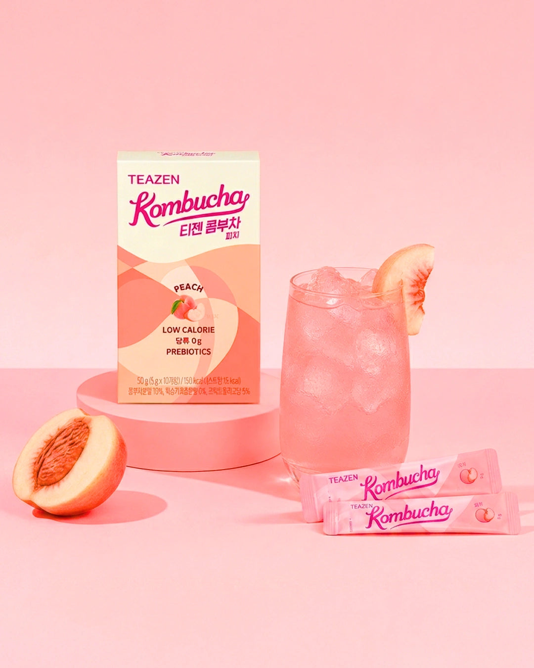 TEAZEN Rombucha Peach flavor probiotic drink packaging shown with a pink iced drink in a glass, two sachets, and peach halves on a soft pink studio background.