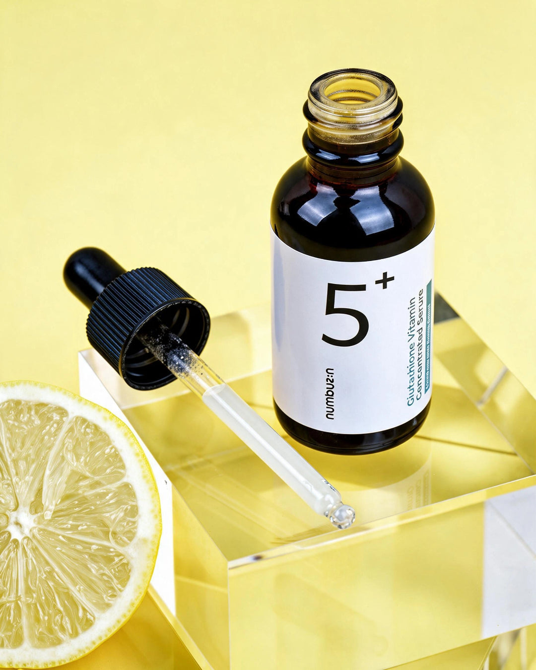 A small amber glass dropper bottle labeled '5+' with a black dropper cap, styled on a reflective yellow surface with a lemon slice beside it. The brand name 'numen-7' is visible on the label.