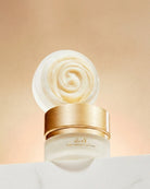 A jar of KAY Solid Volume Care Cream with its lid off, showing a swirl of creamy off-white product inside. The jar has a metallic gold lid and a frosted white base, set against a warm beige background.