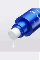 Blue skincare bottle with white cream being squeezed out on a light gray background