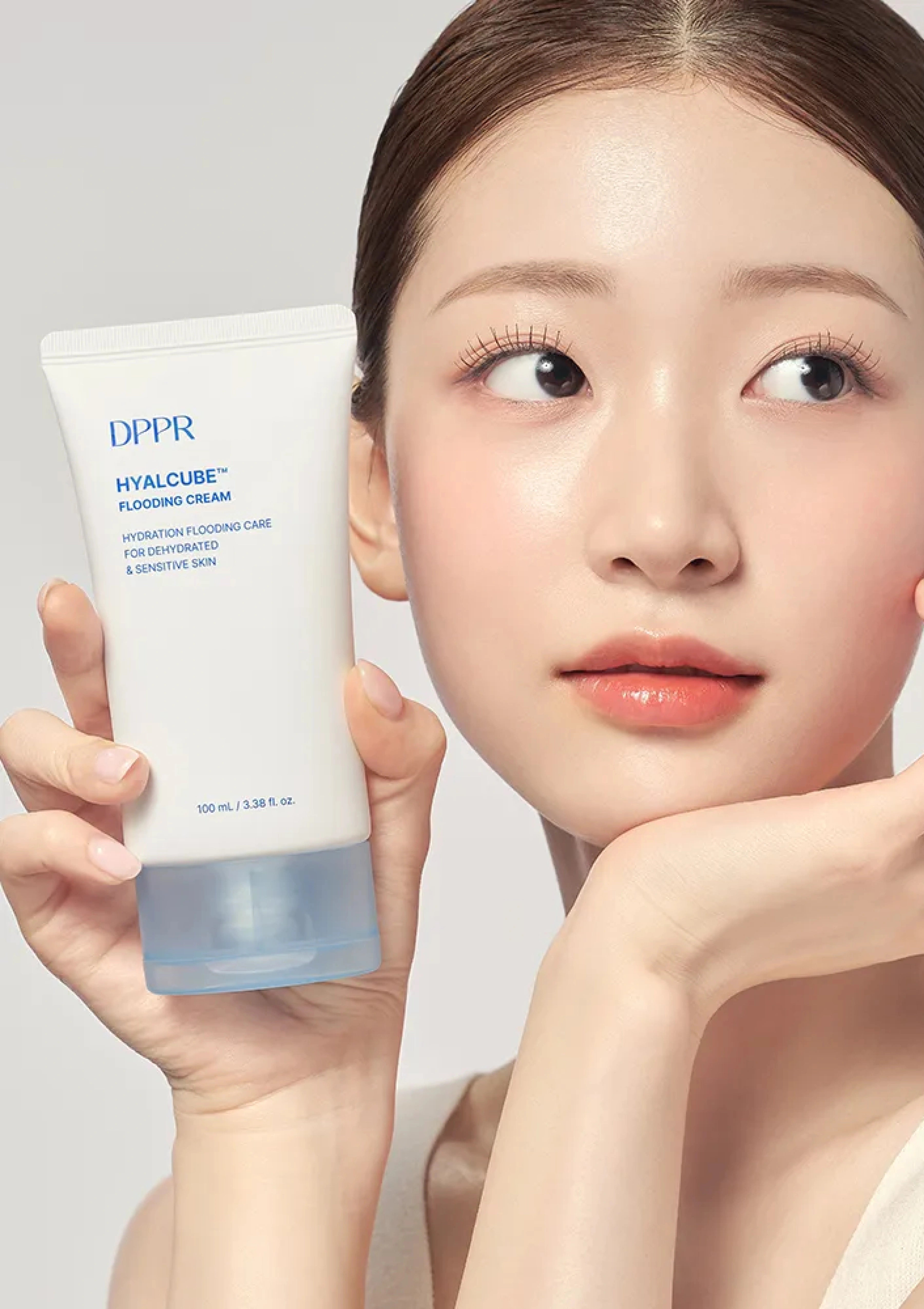 Woman holding a DPPR Hyalcube cream tube against a neutral background