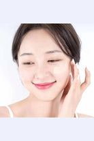 Woman applying cream to her face with a plain background