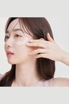 Woman applying cream to her face with a neutral background