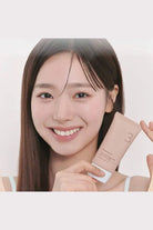 Woman holding a skincare product against a plain background