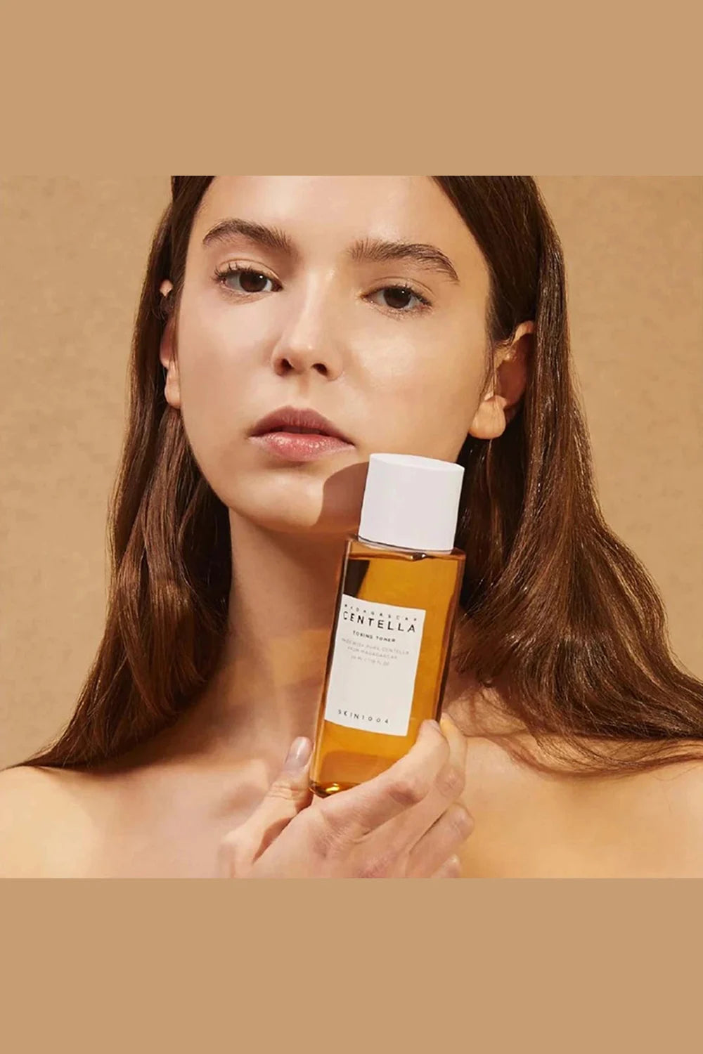 Woman holding a bottle of Caudalie skincare product against a beige background