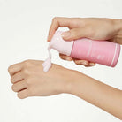 Hand applying pink cream from a bottle labeled 'Medicool' to another hand against a white background