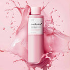 Medicube pink bottle with pink liquid splashes on a pink background