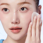 Person using a white cotton pad on their face against a light background