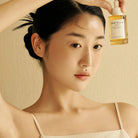 Woman holding a bottle of Centella Asiatica product against a beige background