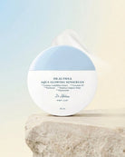 Dr. Alhama Drathea Aqua Glowing Sunscreen in a round white jar with a light blue top section, displayed on a textured stone pedestal against a soft gradient background.